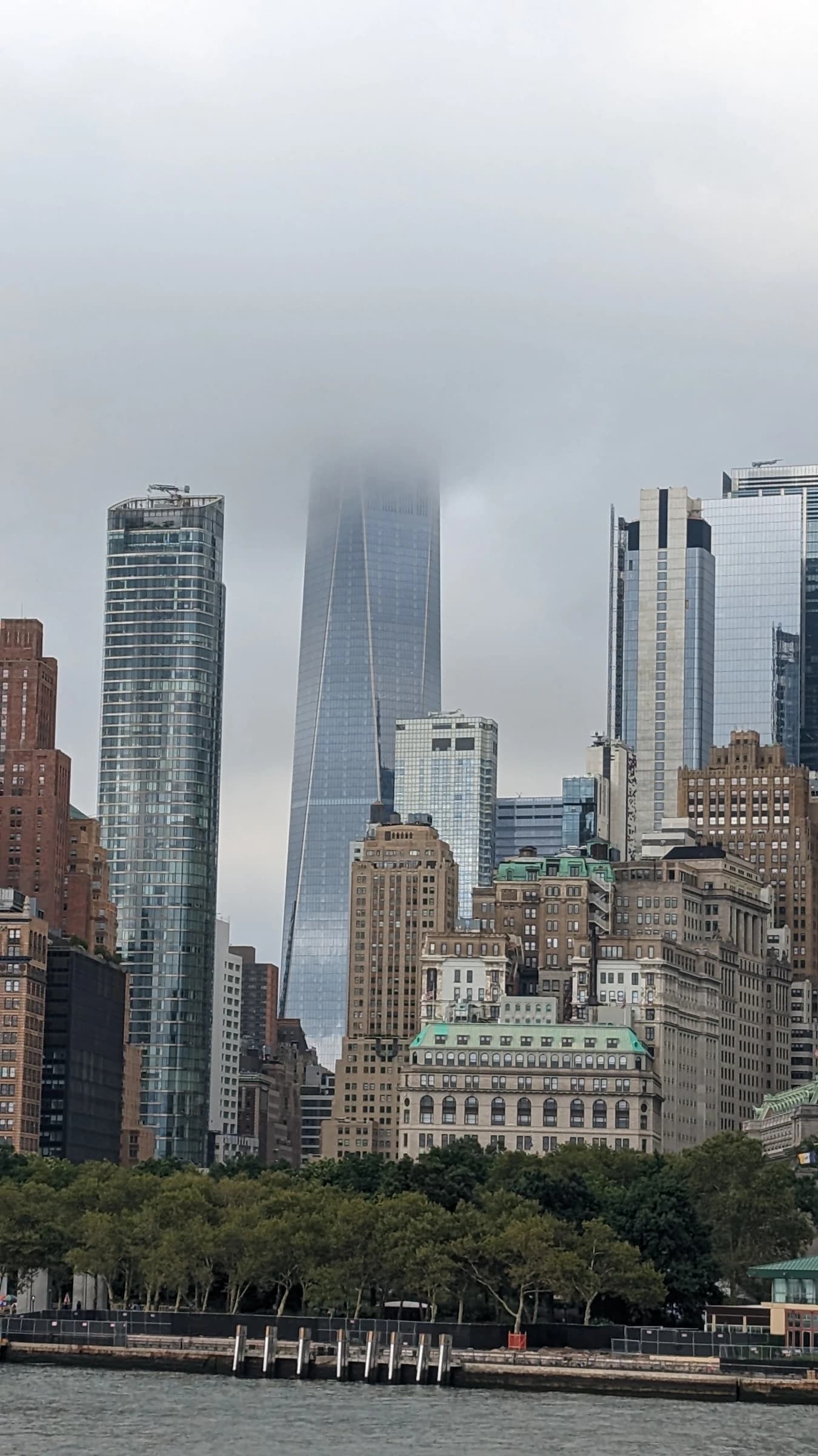 Manhattan's financial district skyline under a cloudy sky, with skyscrapers and One World Trade Center.