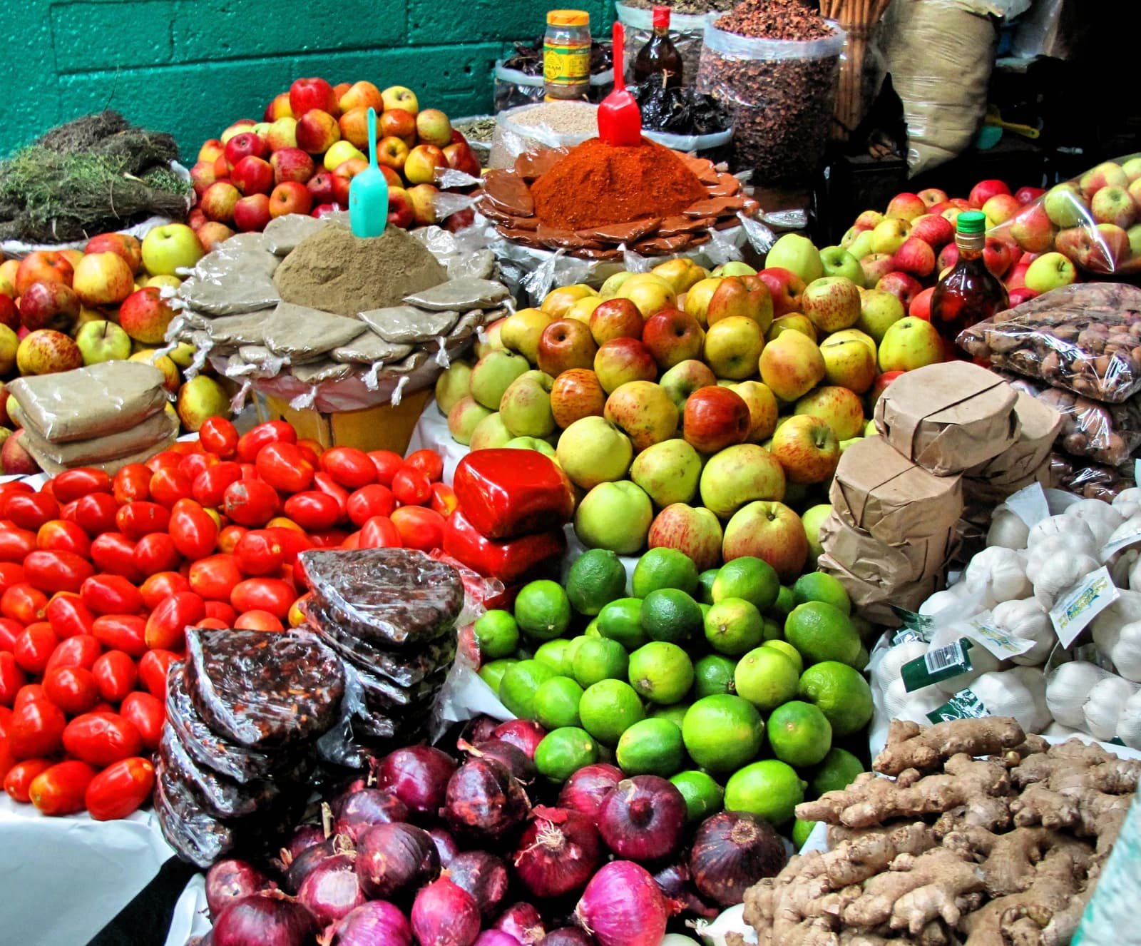 A colorful market stall filled with fresh apples, tomatoes, onions, limes, and spices.
