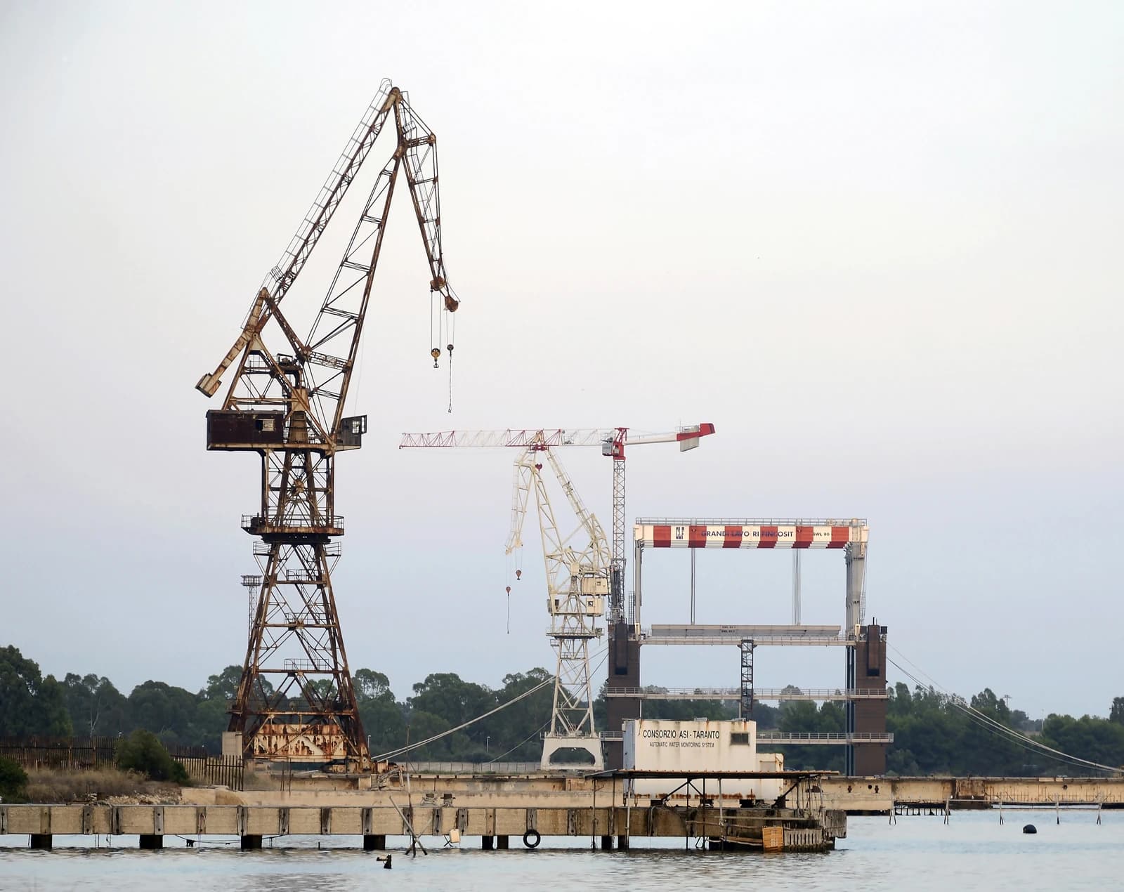 Old cranes stand abandoned at the port of Taranto, Italy.