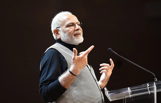 Prime Minister Narendra Modi addressing an audience from a podium with a microphone.