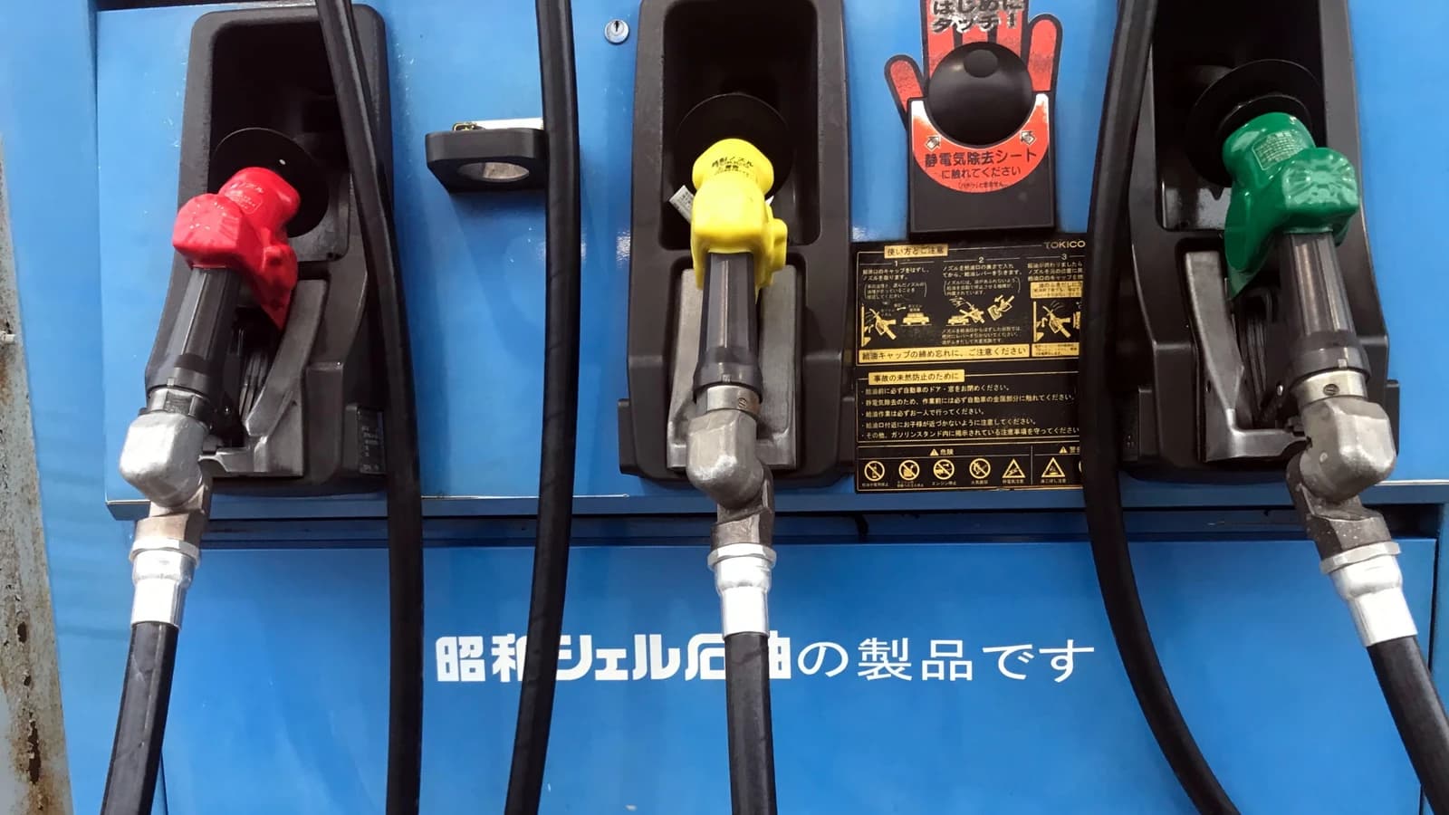 Three colorful fuel dispenser nozzles hanging at a gas station.