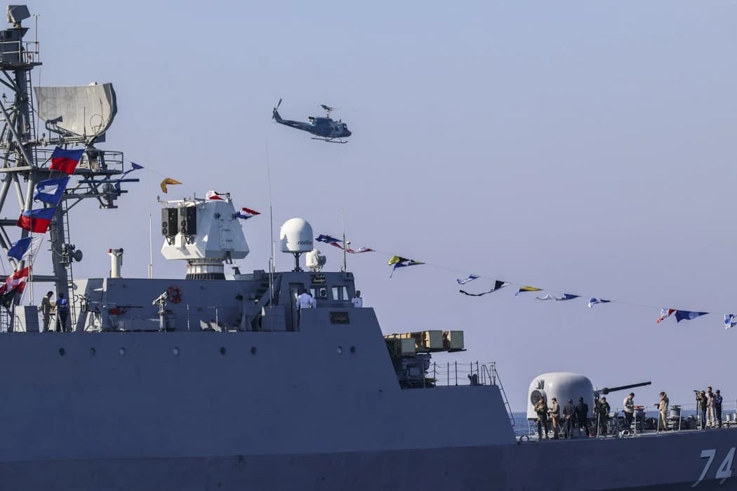 An Iranian Navy ship sails while a helicopter flies above it during a parade.