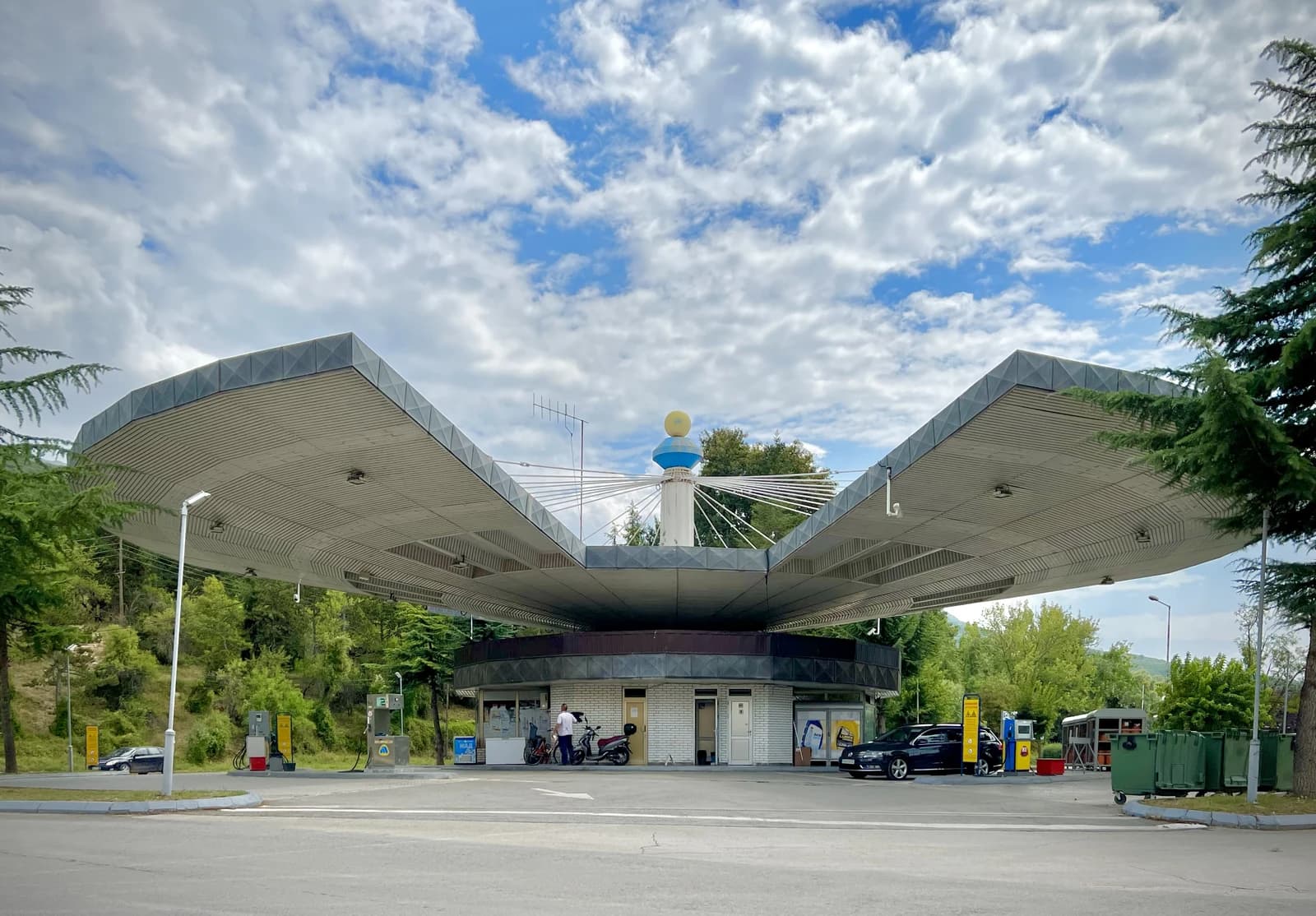 Petrol station with a large, distinctive canopy and several fuel pumps under a cloudy sky.