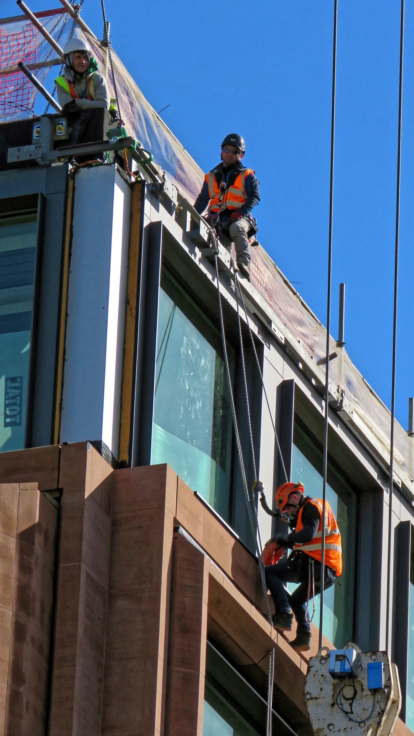 Construction workers wearing hard hats and safety harnesses on a building exterior.