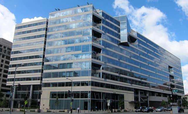 A large modern building with many reflective windows under a blue sky with clouds.