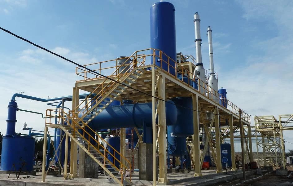 Industrial refining plant with large blue tanks and yellow support structures under a blue sky.