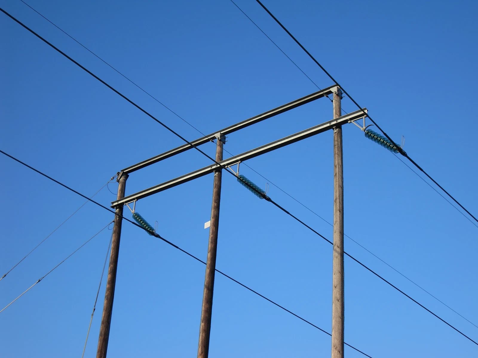 Electric power transmission lines supported by wooden poles against a clear blue sky.