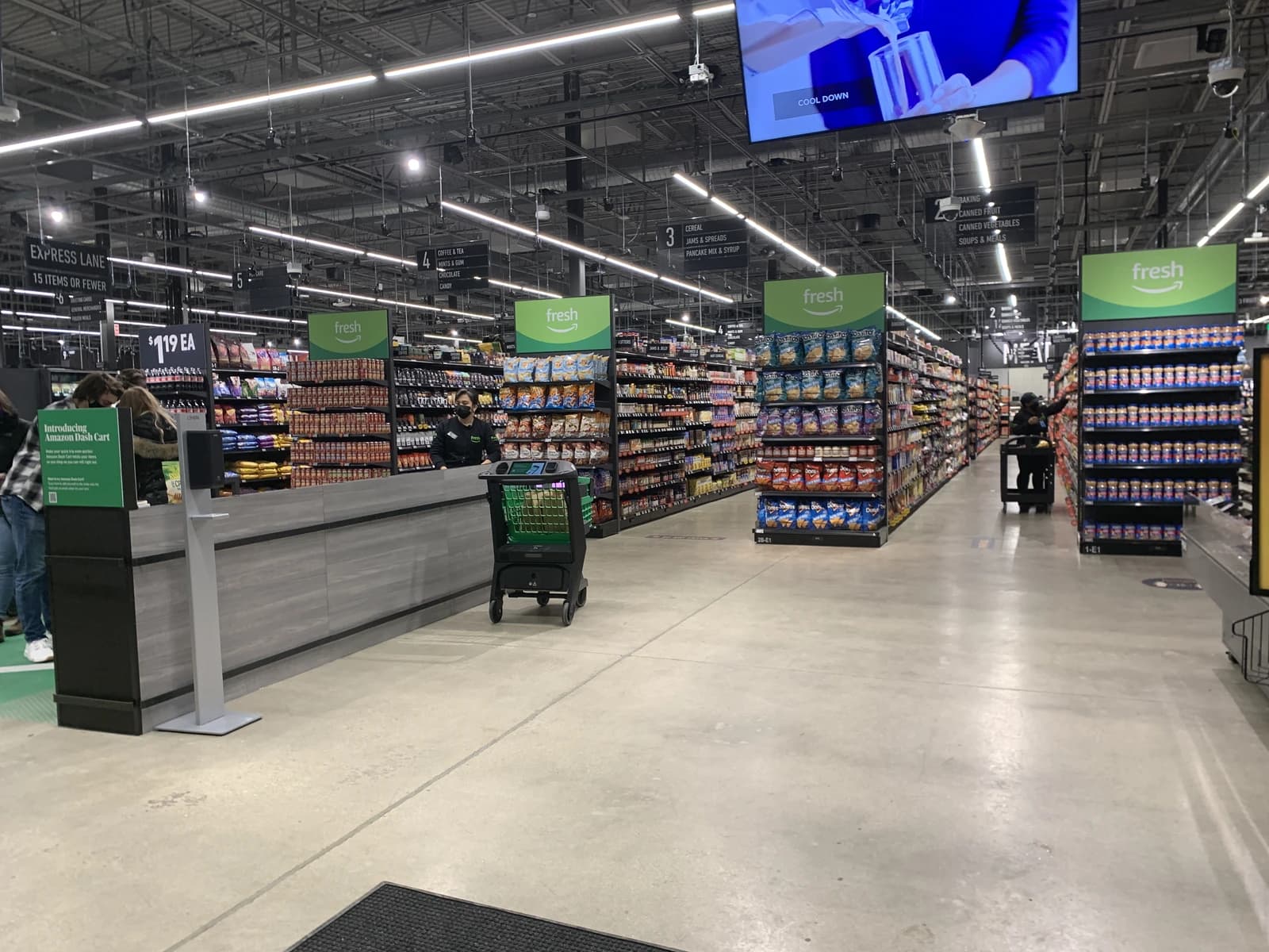 An Amazon Fresh grocery store interior with shelves stocked with products and a checkout counter.