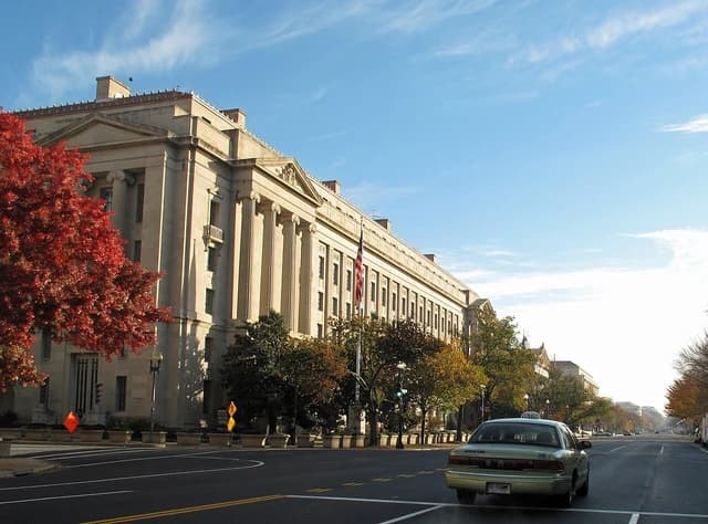 US Department of Justice building in Washington D.C. with a road and red-leaved trees.