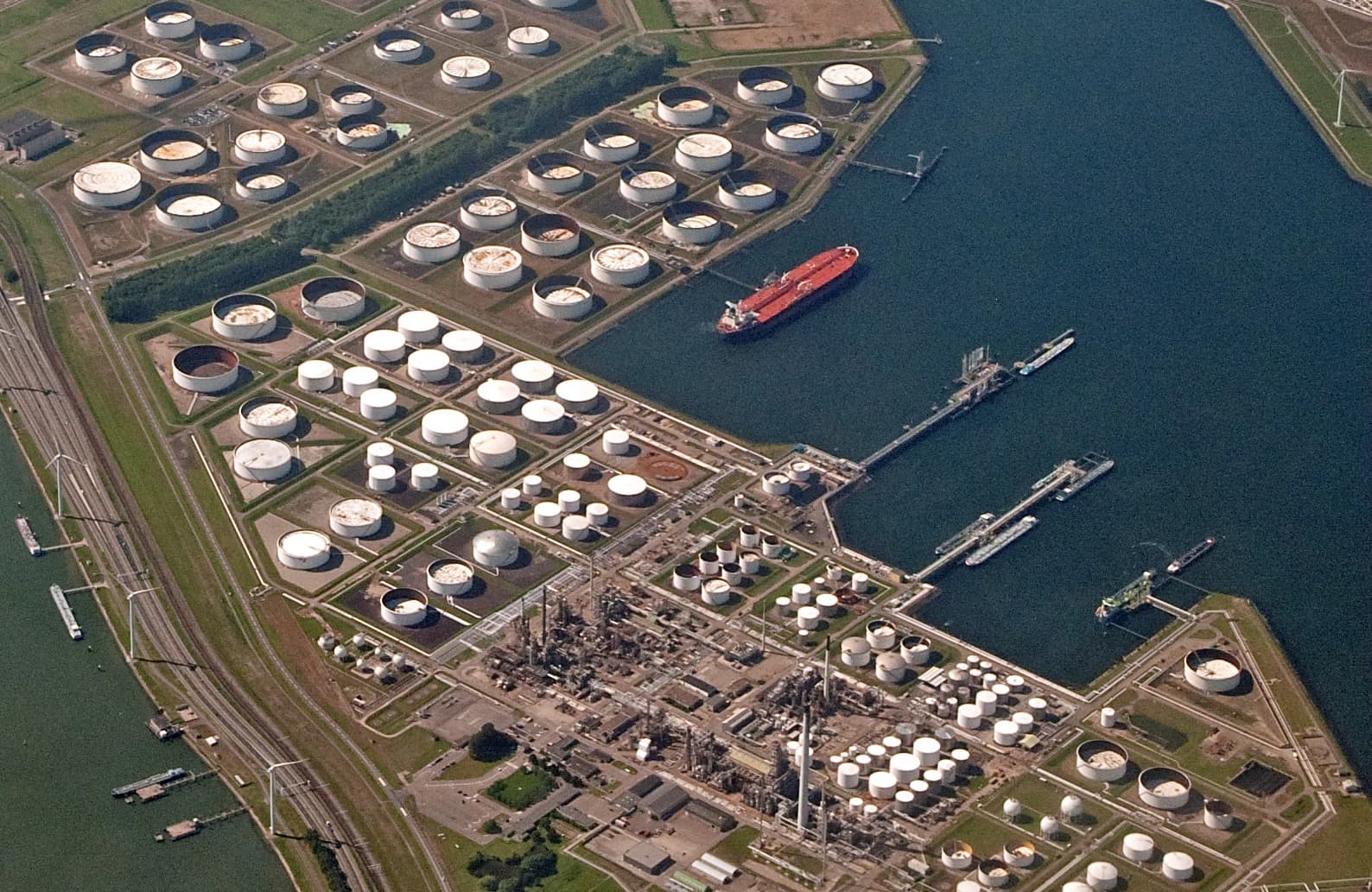 Aerial view of oil storage tanks and a tanker ship docked at a port facility.