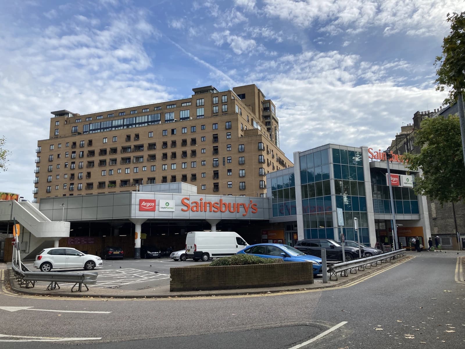 Sainsbury's supermarket entrance and parking lot under a cloudy sky.