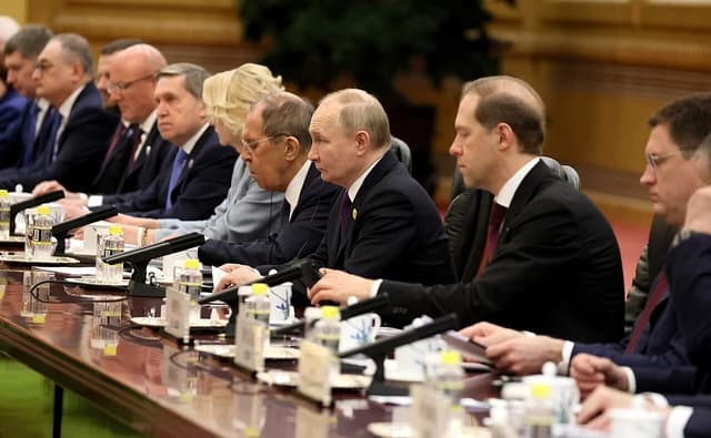 Vladimir Putin, President of Russia, sits at a long table with other Russian delegation members.