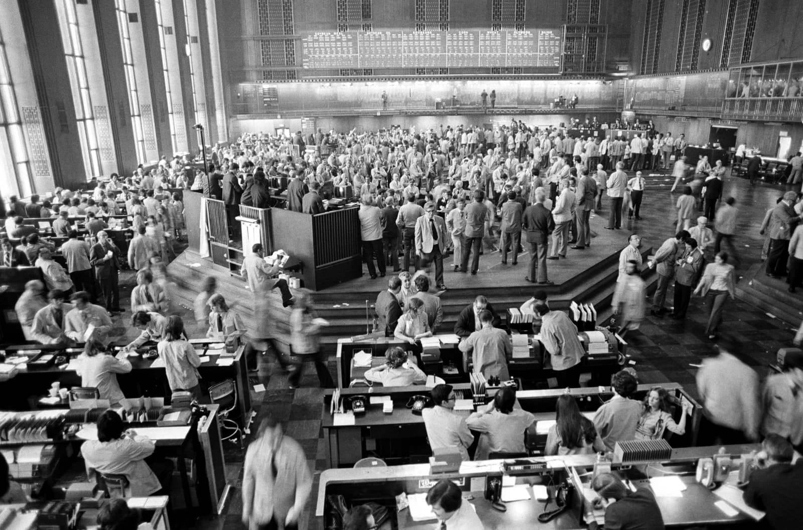 Traders on a busy stock exchange floor, some moving, others at desks.