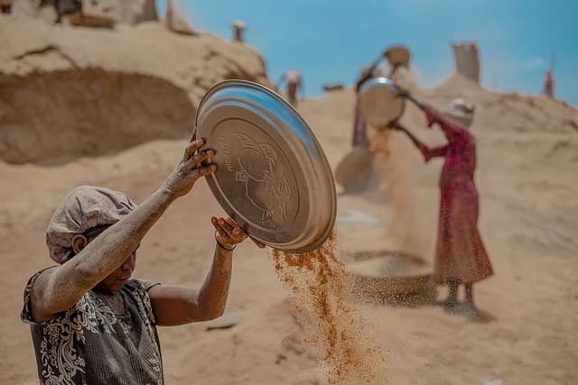 A woman sifts dry grains from a metal tray at an outdoor rice mill.