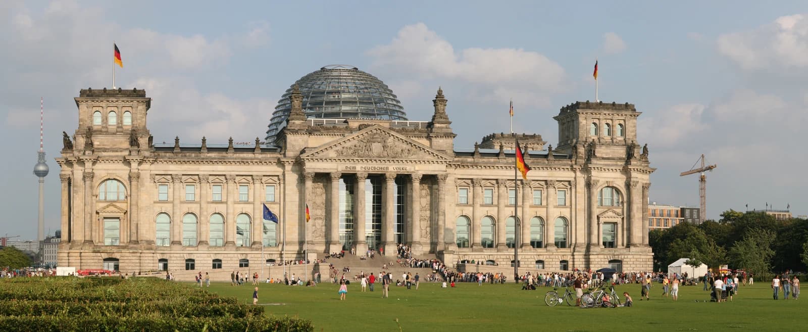 Reichstag building in Berlin, Germany, with German flag flying and people on the grass.