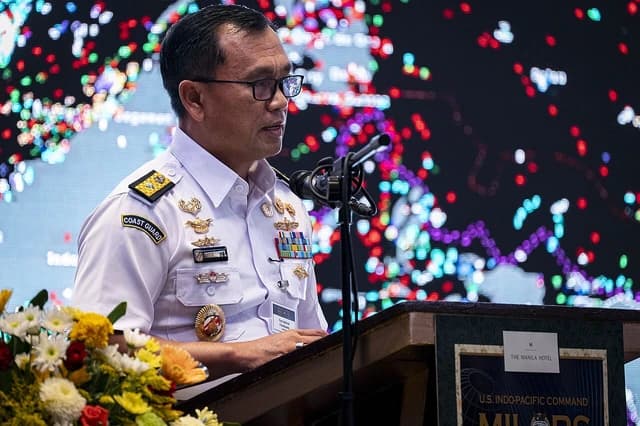 A man in a white military uniform with medals speaks at a podium.