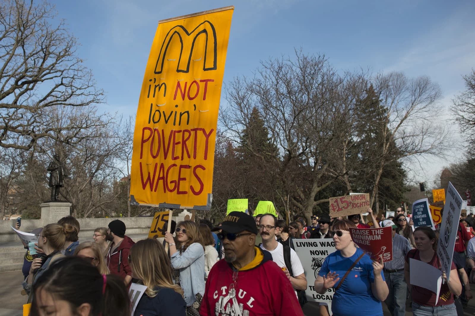 People marching in a street carrying signs during a minimum wage protest.