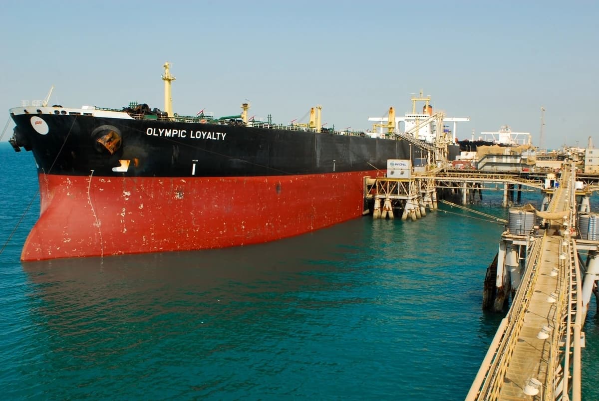 An oil tanker named Olympic Loyalty docked at a large oil terminal with jetties over blue water.