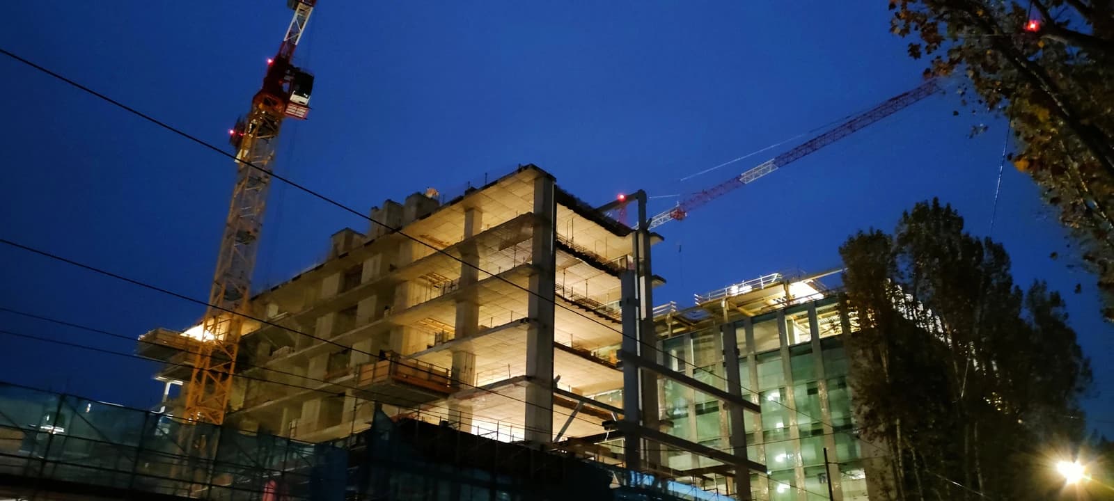 Construction site of a multi-story building illuminated at night with cranes visible.