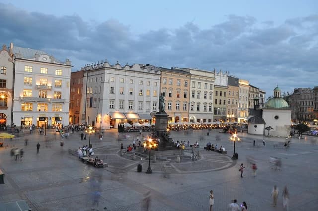 Krakow Main Market Square at dusk with historic buildings and faint outlines of people.