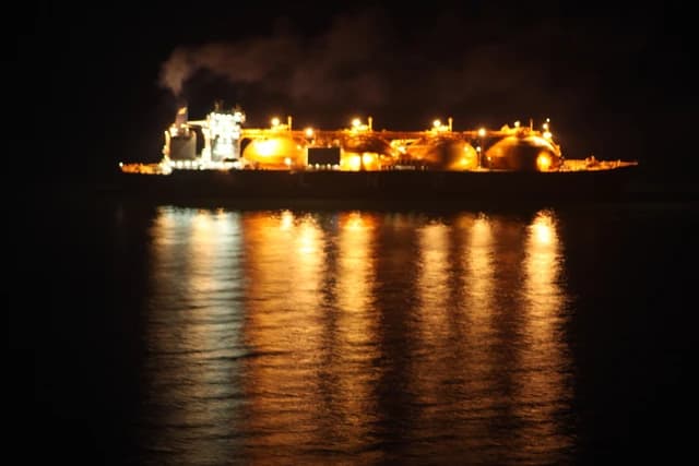 LNG carrier ship illuminated at night, with its lights reflecting on the water.