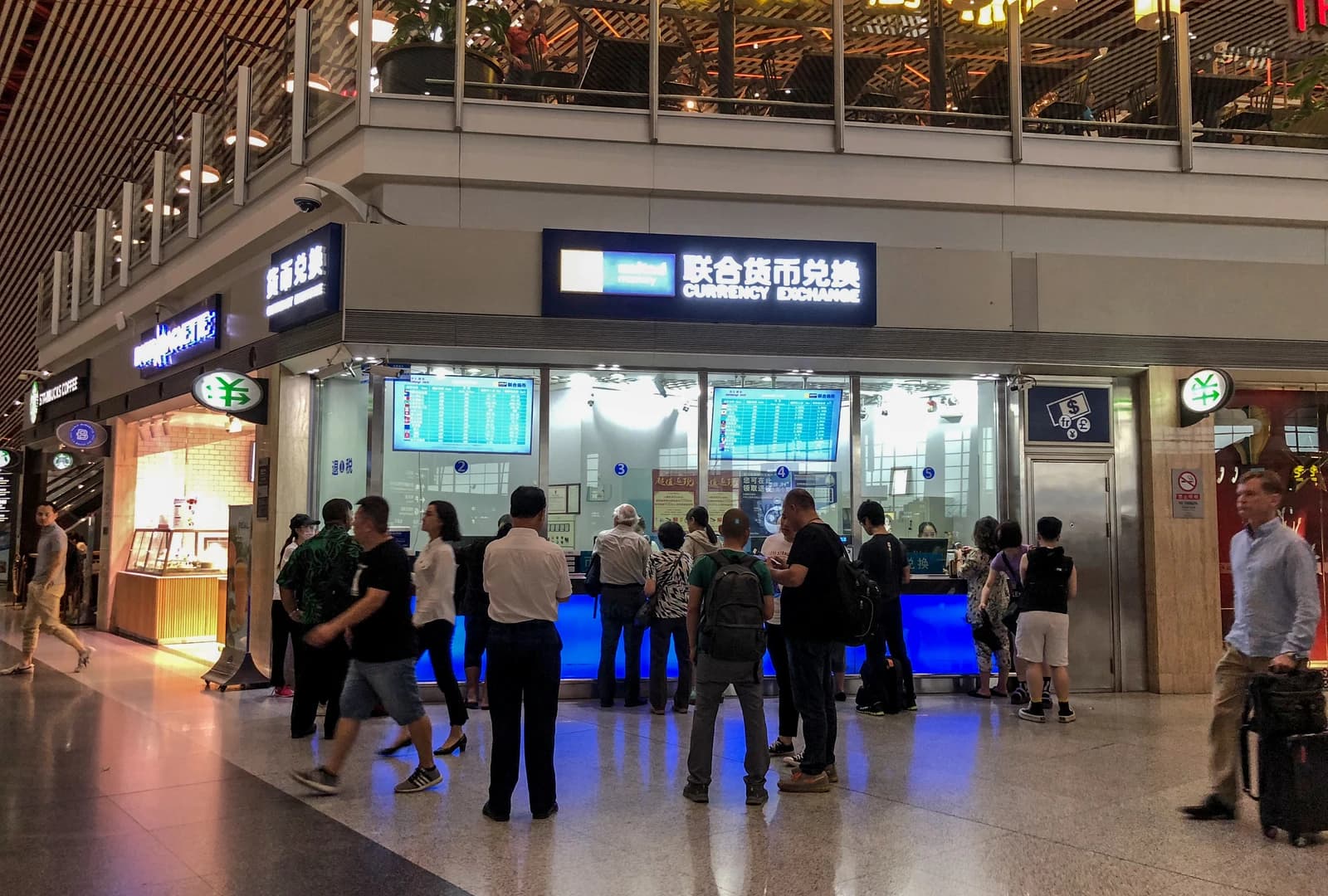People standing in line at a currency exchange booth inside a busy airport.