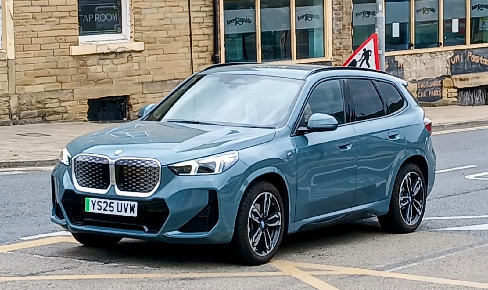 2025 BMW iX1 electric car in teal driving on a street.