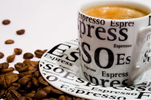 Espresso cup filled with coffee sits on a saucer surrounded by coffee beans.