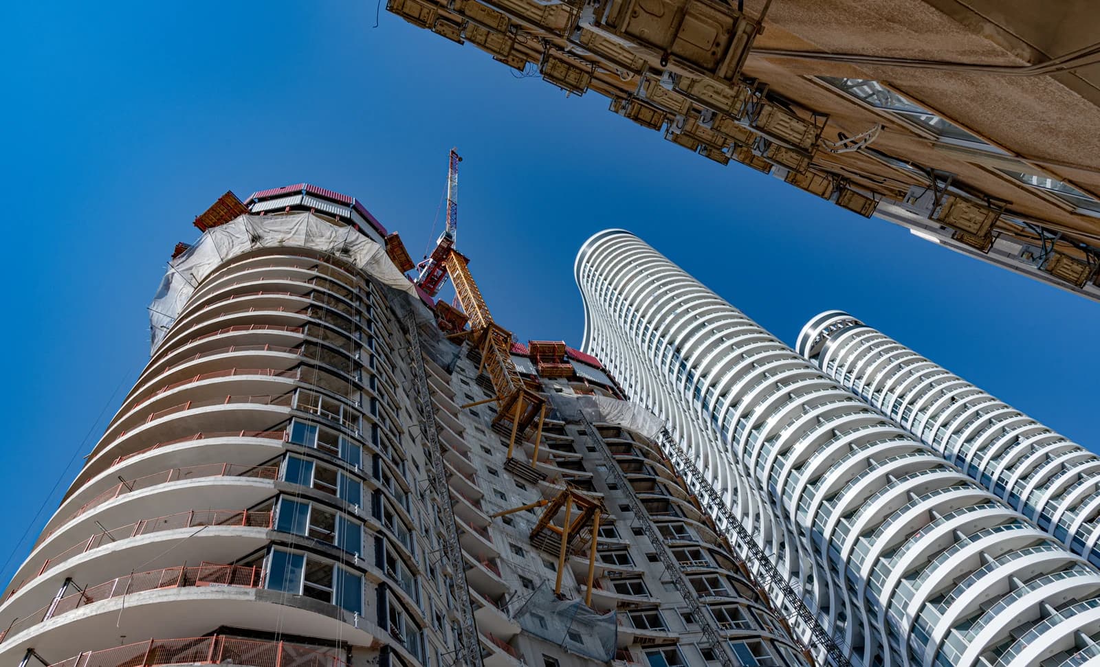 Skyscrapers under construction, with a crane visible, alongside completed modern residential towers.