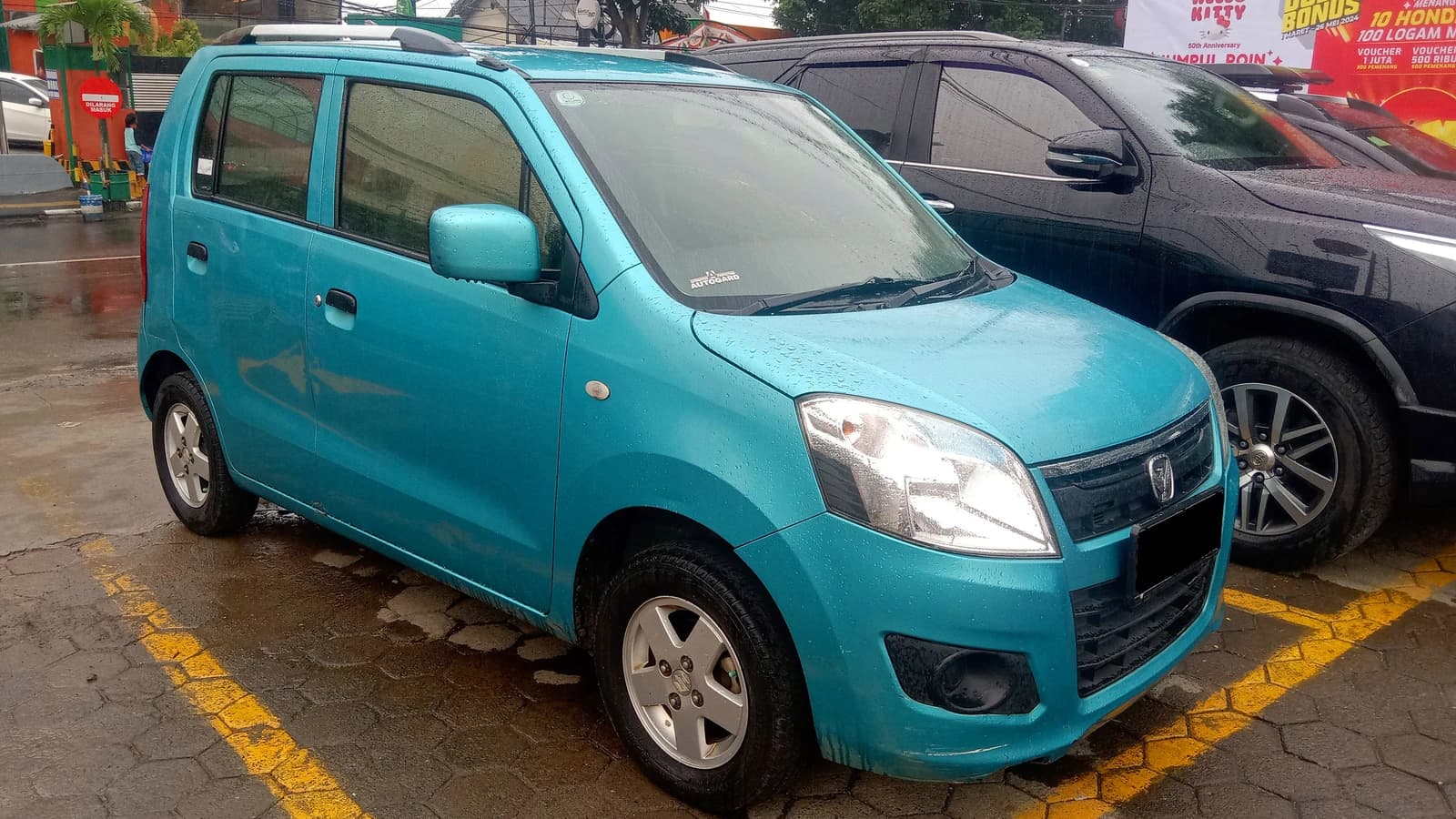 Turquoise 2014 Suzuki Karimum Wagon R 1.0 GL parked on a wet street in Bandung.