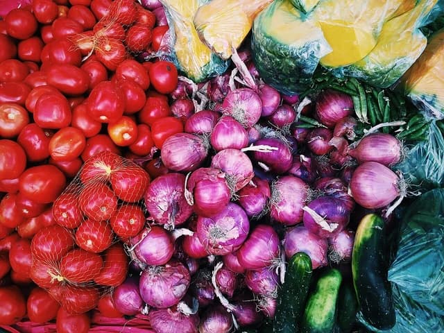 Close-up of fresh tomatoes, red onions, and cucumbers on display at a market.