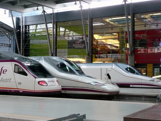 Three white and purple high-speed trains parked at a station platform.