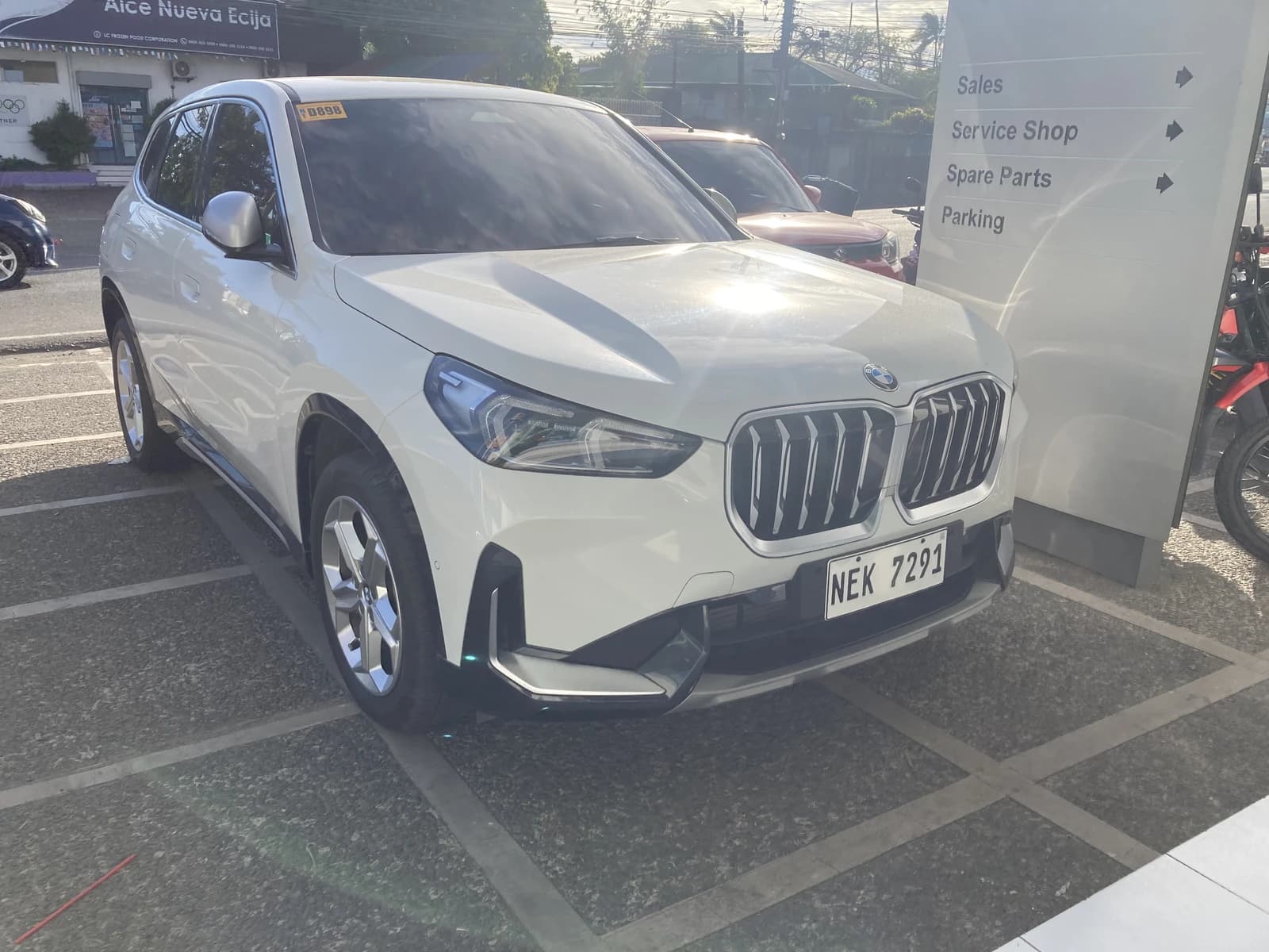 White BMW X1 U11 sDrive18d parked with a sign indicating sales and service.