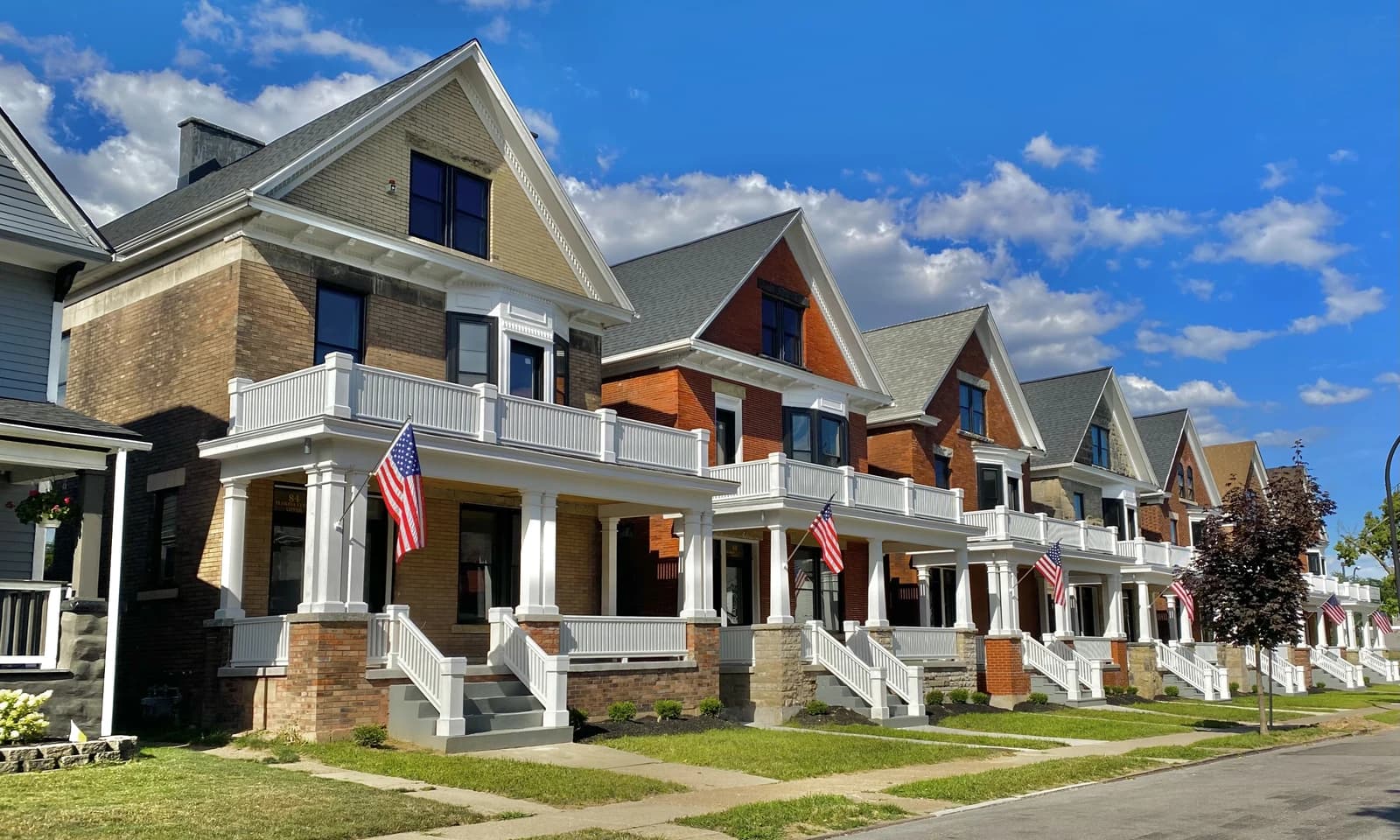 Row of historic brick and siding homes with front porches and American flags in Buffalo, New York.
