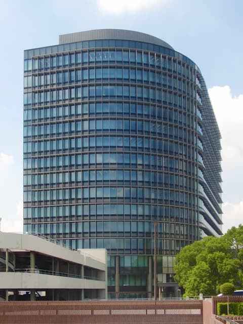 The glass and steel headquarters building of Toyota Motor Corporation stands under a blue sky.