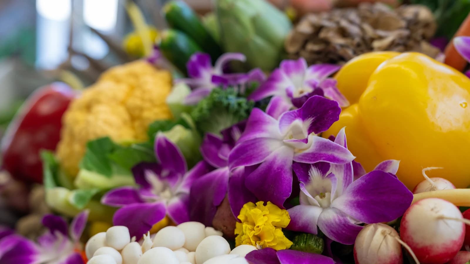 Colorful display of fresh vegetables, including bell peppers, cauliflower, mushrooms, and purple orchids.