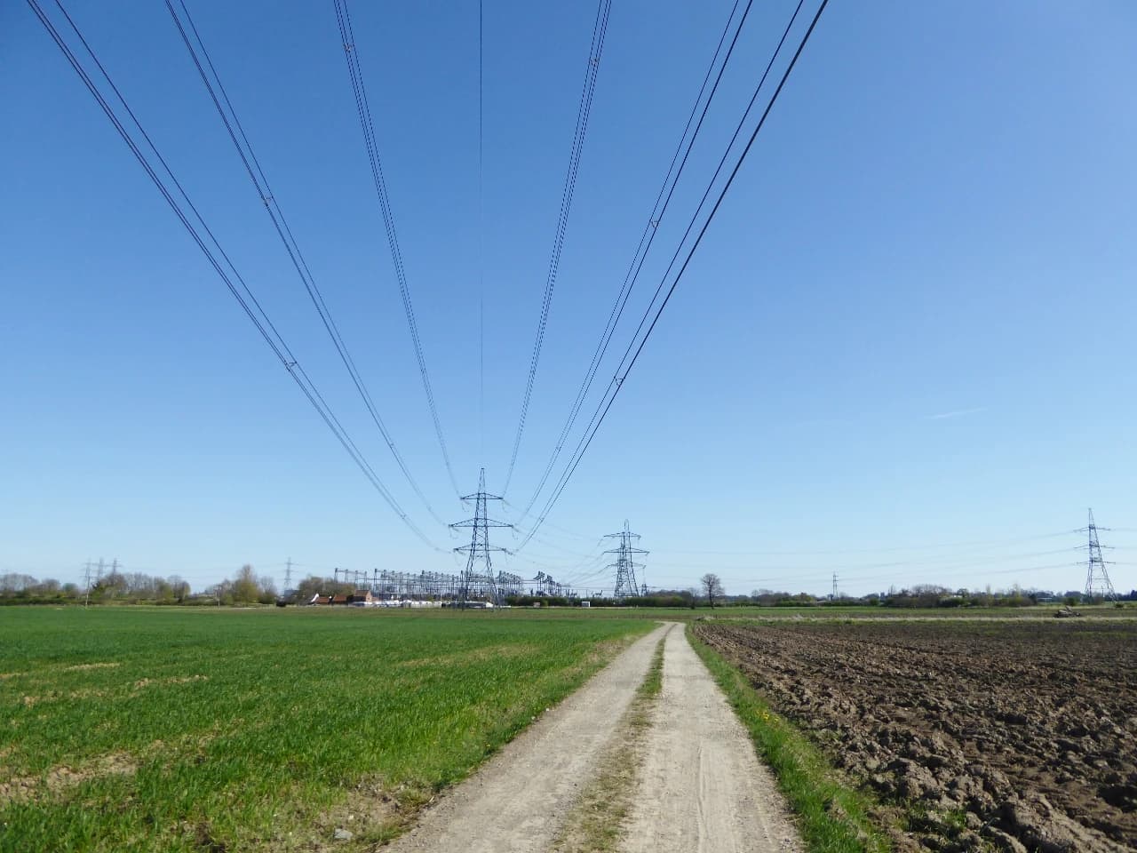 Pylons and overhead power lines extend across a rural landscape near a substation.