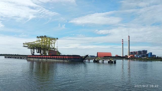 Coal loading equipment at a power plant dock with two tall chimneys in the background.