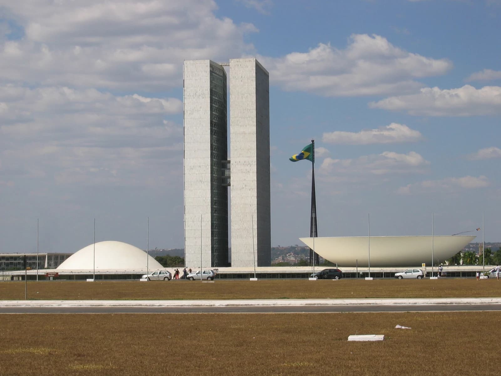 The Brazilian National Congress building, with two towers and two domes, under a cloudy sky.