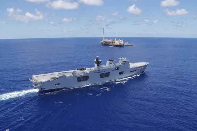 Brazilian Navy ship Atlântico (A140) sailing on the ocean with an oil platform in the background.