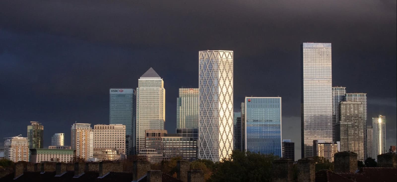 Skyscrapers of Canary Wharf, London, illuminated against a dramatic dark sky.