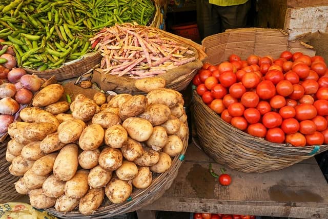 Tomatoes, potatoes, beans, and onions in baskets at a market stall.