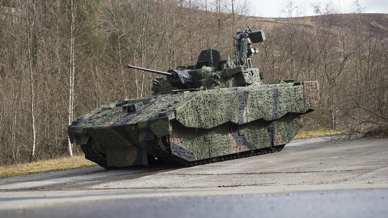 An AJAX armoured fighting vehicle in camouflage, parked on an asphalt surface.
