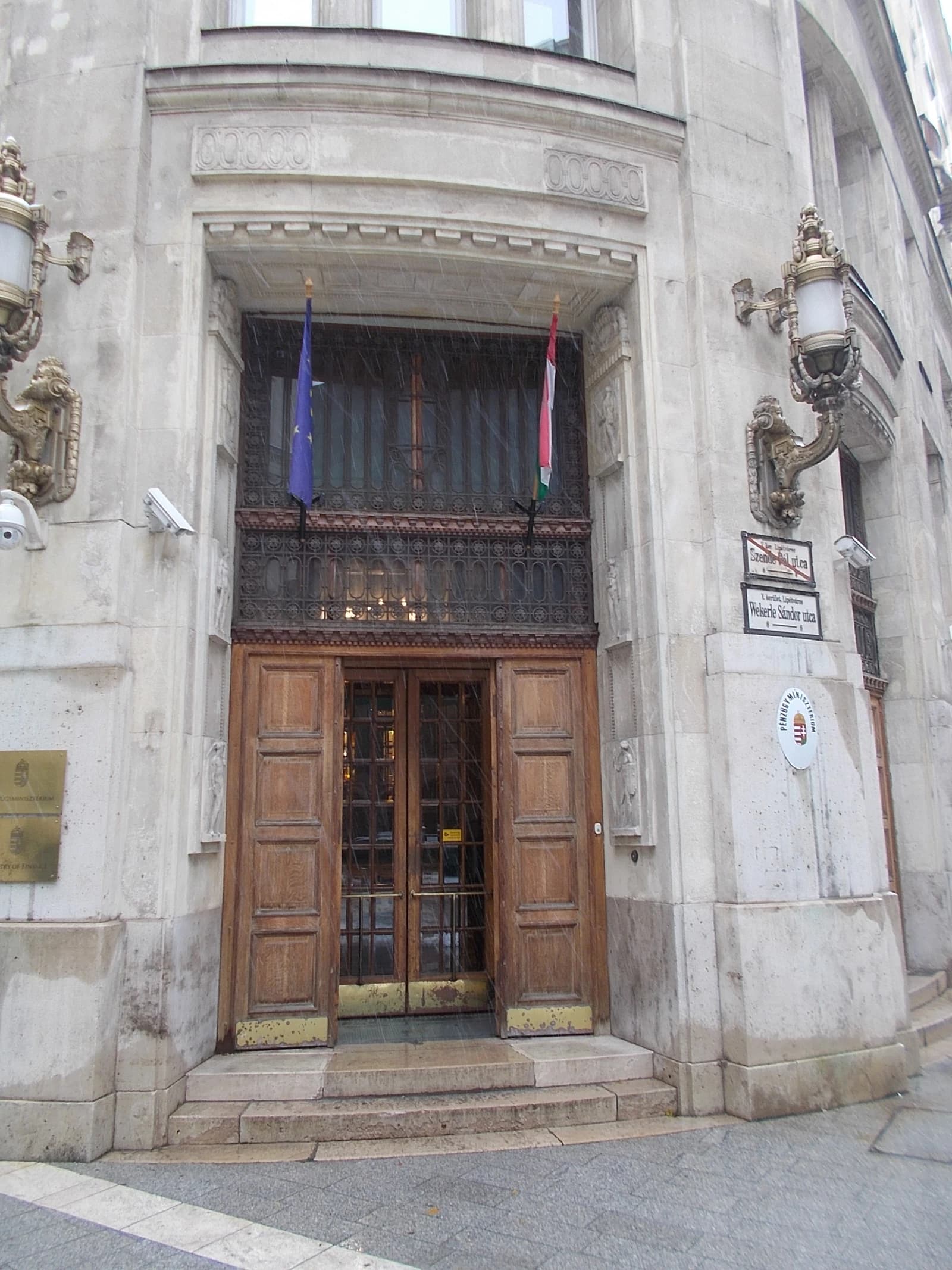 Entrance of the Ministry of Finance building in Hungary with EU and Hungarian flags displayed.