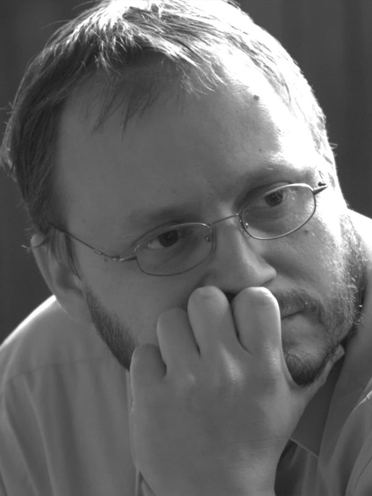 András Kármán, an individual with glasses and a beard, looks thoughtfully towards the camera.