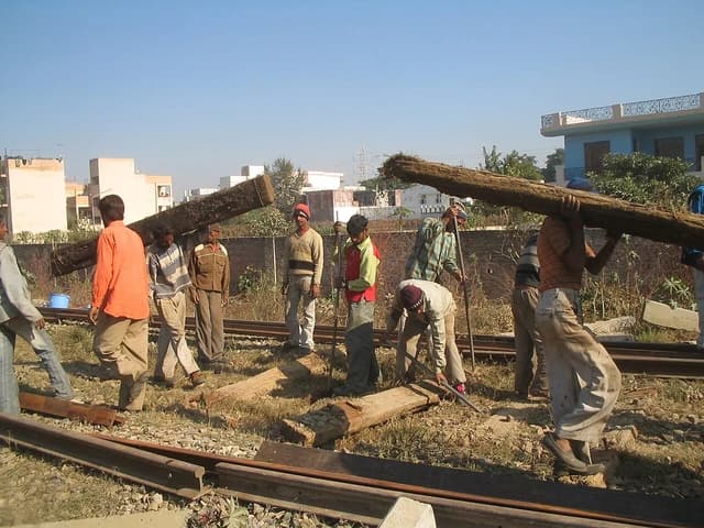 Indian railway workers carry large wooden railway ties and perform track maintenance.
