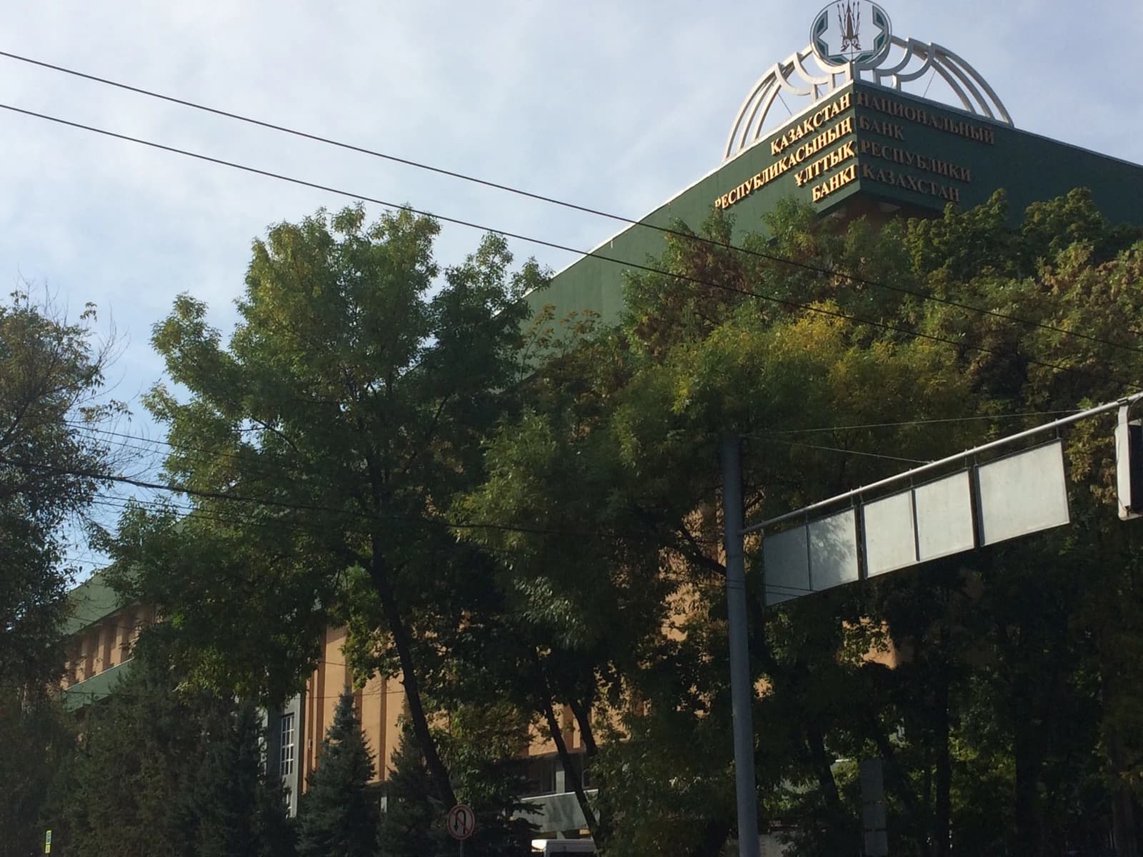 Exterior of the National Bank of the Republic of Kazakhstan building in Almaty, partially obscured by trees.