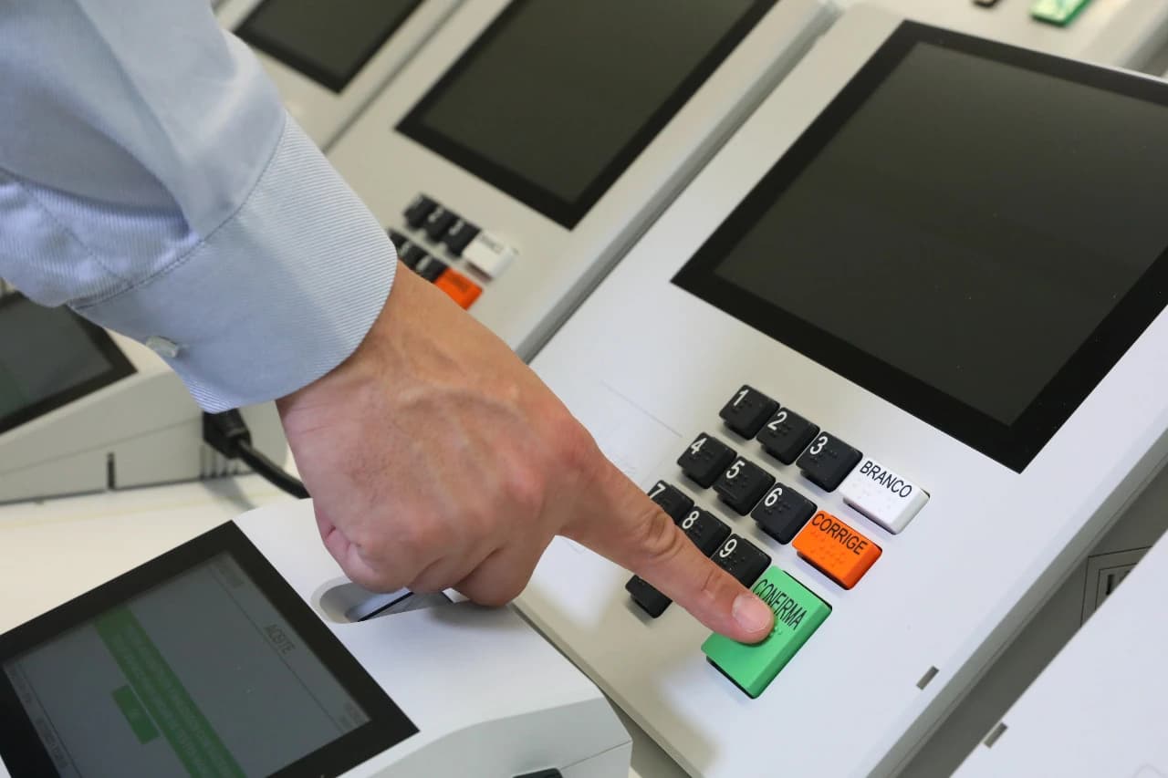 Person's hand pressing the 'Confirma' button on a Brazilian electronic voting machine.