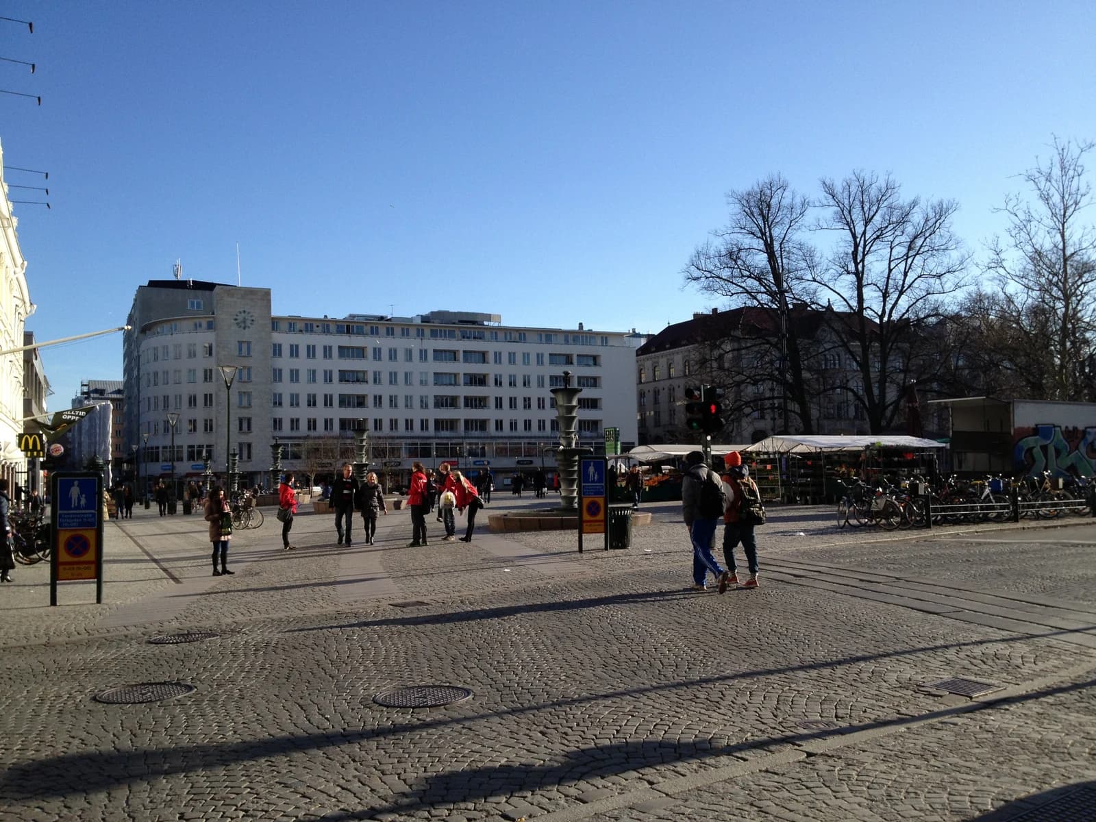 People walk across Gustav Adolfs Torg in Malmö, Sweden, on a sunny day.