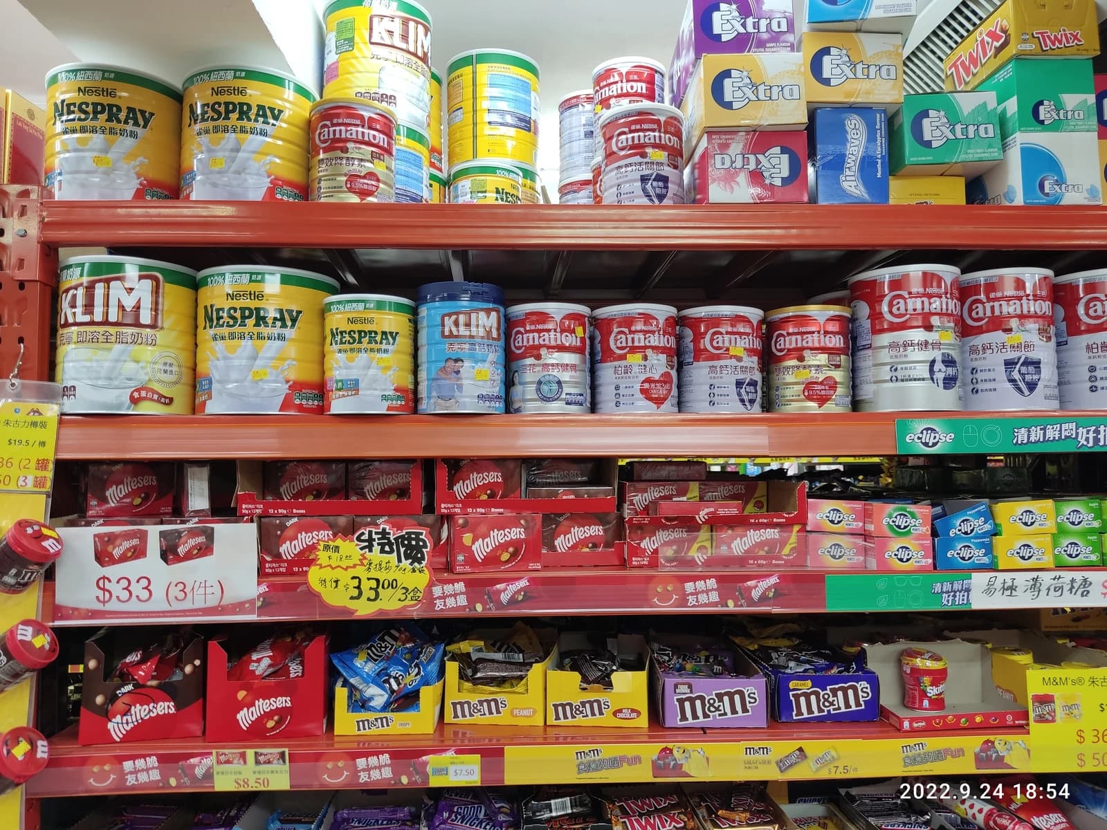 Cans of Nestle NESPRAY and KLIM milk powder on a supermarket shelf.